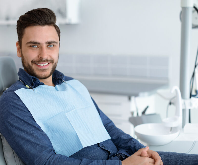 Smiling male dental patient wearing a protective bib while seated in a treatment chair at a cosmetic dentistry office in Bethesda, MD