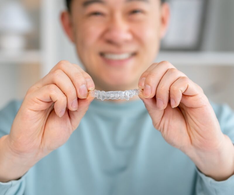 Smiling adult holding a clear Invisalign aligner during treatment in Bethesda, MD
