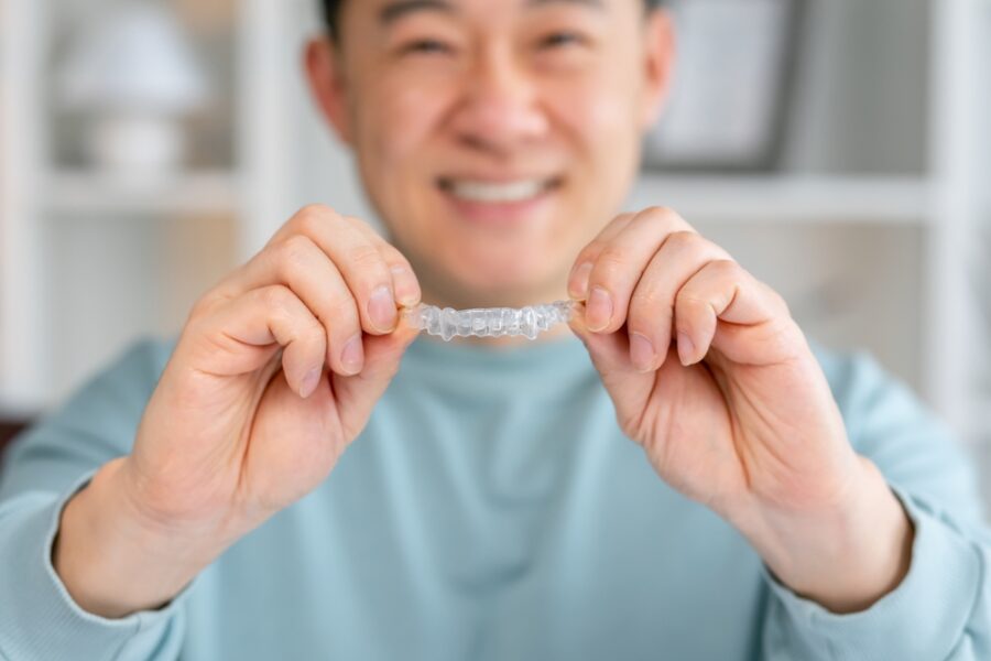 Smiling adult holding a clear Invisalign aligner during treatment in Bethesda, MD